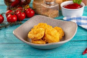 A bowl of fried food on a table next to a bottle of ketchup photo