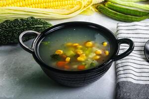 A bowl of soup with corn, carrots and other vegetables photo