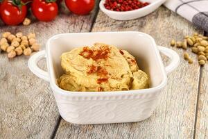 A bowl of hummus with a spoon and a bowl of tomatoes photo