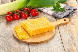 A wooden cutting board with cheese and vegetables photo