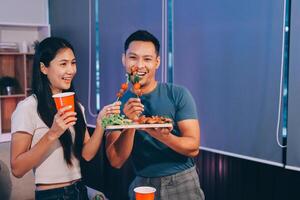 A couple eating food while standing in front of a table photo