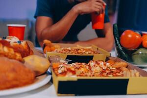 A man sitting at a table with two boxes of pizza and a drink photo