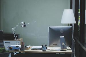 A desk with a computer, a lamp, and a clock photo