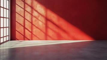 Bright sunlight casts long shadows across a vibrant red wall in an empty room with a polished concrete floor during the afternoon photo