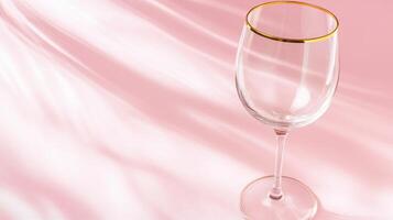 Elegant transparent glass with a golden rim placed on a soft pink backdrop, capturing a touch of sophistication and simplicity in a well-lit setting photo