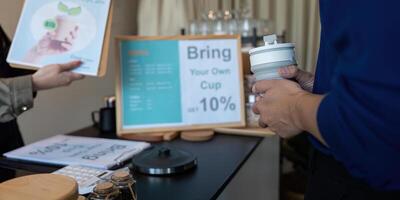 Sustainability and Eco-Friendly Practices. A customer in a cafe holds a reusable cup, promoting sustainable coffee consumption. photo