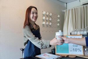 Promoting Eco-Conscious Choices. A barista hands a reusable cup to a customer to support sustainability. photo