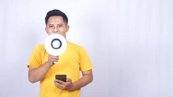 Portrait of Asian man holding mobile phone and shouting on megaphone isolated on white background photo