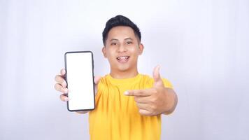 Happy Asian man showing mobile phone blank screen mock up and pointing at it isolated on white background photo