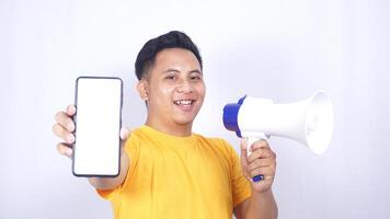 Smiling Asian man holding megaphone and showing mobile phone blank screen mock up isolated on white background photo