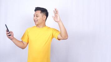 Happy Asian man looking at mobile phone and making greeting gesture isolated on white background photo