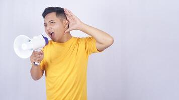 Asian man shouting on megaphone and placing his hand open behind his ear isolated on white background photo