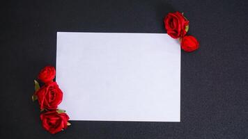 A beautiful artificial or fake red rose with blank paper for copy space isolated on black background photo