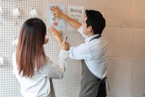 Sustainability and Teamwork. Staff members enthusiastically promote eco-friendly practices at a cafe by hanging up a poster about using personal cups. photo