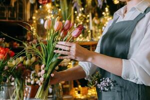 A florist works preparing beautiful floral arrangement. Various flowers and materials lie on table, emphasizing the artistic and inspiring atmosphere associated with floral design and presentation. photo