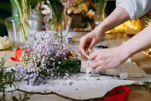 A florist works on preparing beautiful floral arrangement. Various flowers and materials lie table, emphasizing the artistic and inspiring atmosphere associated with floral design and presentation photo
