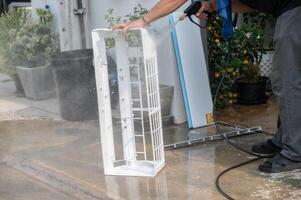 Technician using high pressure water gun for cleaning air conditioner frame. photo