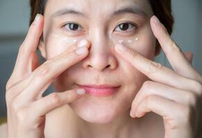 Asian woman applying anti aging cream on her under eyes. The anti aging cream is using to reducing, masking or preventing signs of skin aging. photo
