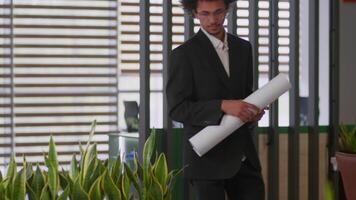 Ethnic architect developer male guy coming in office with architecture plan African American man businessman business engineer walking in company with blueprint construction building sketch analyze video