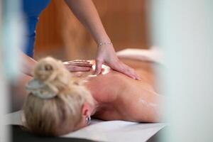 Relaxing Back Massage in a Spa Setting. A professional massage therapist in a blue uniform provides a relaxing back massage to a client lying on a massage table. photo