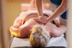 Relaxing Back Massage in a Spa Setting. A professional massage therapist in a blue uniform provides a relaxing back massage to a client lying on a massage table. photo