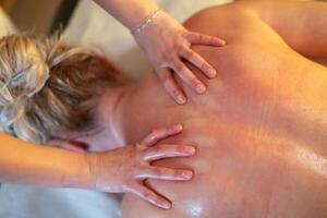 Relaxing Back Massage in a Spa Setting. A professional massage therapist in a blue uniform provides a relaxing back massage to a client lying on a massage table. photo