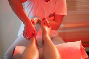 Foot Massage Therapy in a Relaxing Spa Setting. A professional massage therapist in a white uniform provides a soothing foot massage to a client in a calm and serene spa environment photo