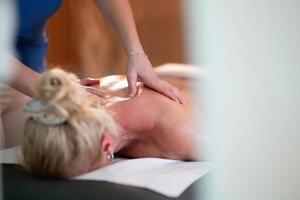 Relaxing Back Massage in a Spa Setting. A professional massage therapist in a blue uniform provides a relaxing back massage to a client lying on a massage table. photo