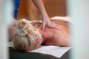 Relaxing Back Massage in a Spa Setting. A professional massage therapist in a blue uniform provides a relaxing back massage to a client lying on a massage table. photo