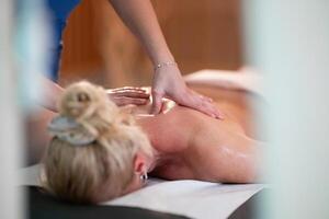 Relaxing Back Massage in a Spa Setting. A professional massage therapist in a blue uniform provides a relaxing back massage to a client lying on a massage table. photo