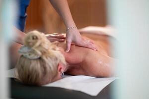 Relaxing Back Massage in a Spa Setting. A professional massage therapist in a blue uniform provides a relaxing back massage to a client lying on a massage table. photo