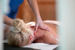 Relaxing Back Massage in a Spa Setting. A professional massage therapist in a blue uniform provides a relaxing back massage to a client lying on a massage table. photo