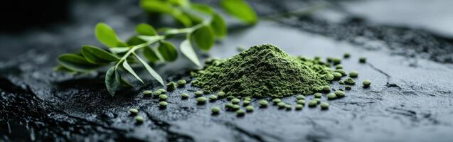 Moringa powder displayed on a dark surface with fresh leaves nearby photo