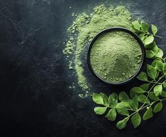 Moringa powder displayed with fresh leaves on a dark surface photo