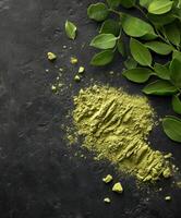 Moringa powder with fresh leaves on a dark surface photo