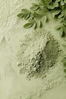Moringa powder spread on green surface with fresh leaves nearby photo