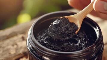 A person is holding a wooden spoon over a jar of black clay photo