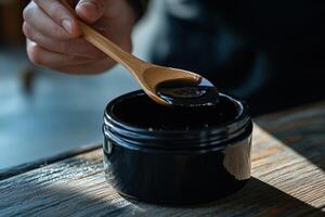 A person is holding a spoon over a jar of black paste photo