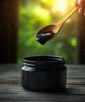 Black charcoal paste in jar with wooden spoon on wooden table photo