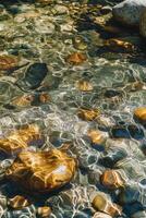 Clear river water reflecting light on smooth rocks below photo