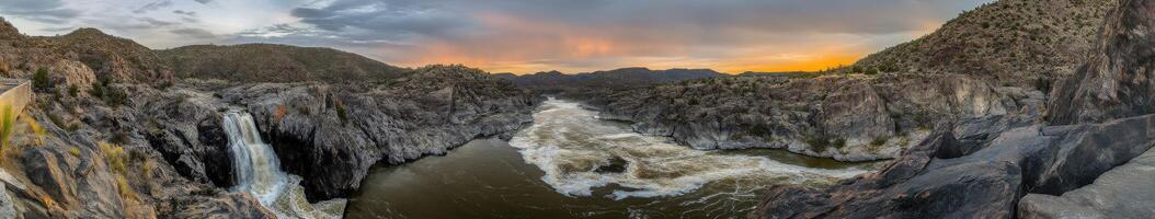 Panoramic view of a mountain river flowing through rugged terrain during sunset with vibrant colors in the sky photo