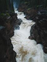 Mountain river cascading through rocky cliffs in a lush forest setting during overcast weather photo