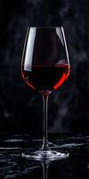 Elegant red wine glass filled with rich garnet liquid on dark marble surface photo