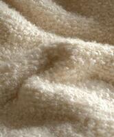 Soft and textured boucle fabric in neutral tones placed on a surface illuminated by warm natural light during the afternoon photo