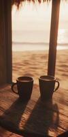 Warm coffee mugs on a beachside table at sunset with calming ocean waves in the background photo