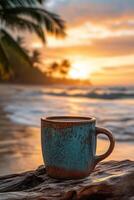 Warm sunrise over the ocean with a colorful coffee mug resting on a wooden log in a tropical beach setting photo