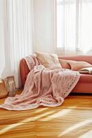 Cozy living room corner featuring a pink sofa adorned with a textured blanket and a warm atmosphere in natural light photo
