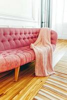 Cozy living room featuring a pink tufted sofa with a knitted blanket draped over it in a bright and airy space photo