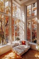 Cozy corner in a sunlit room with autumn trees visible through large windows photo