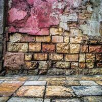 Textured stone wall in vibrant colors beside a weathered pavement in an urban area during daylight photo